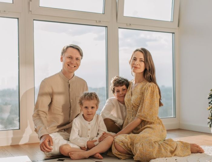 A cheerful family of four sitting together on the floor of a sunlit living room.