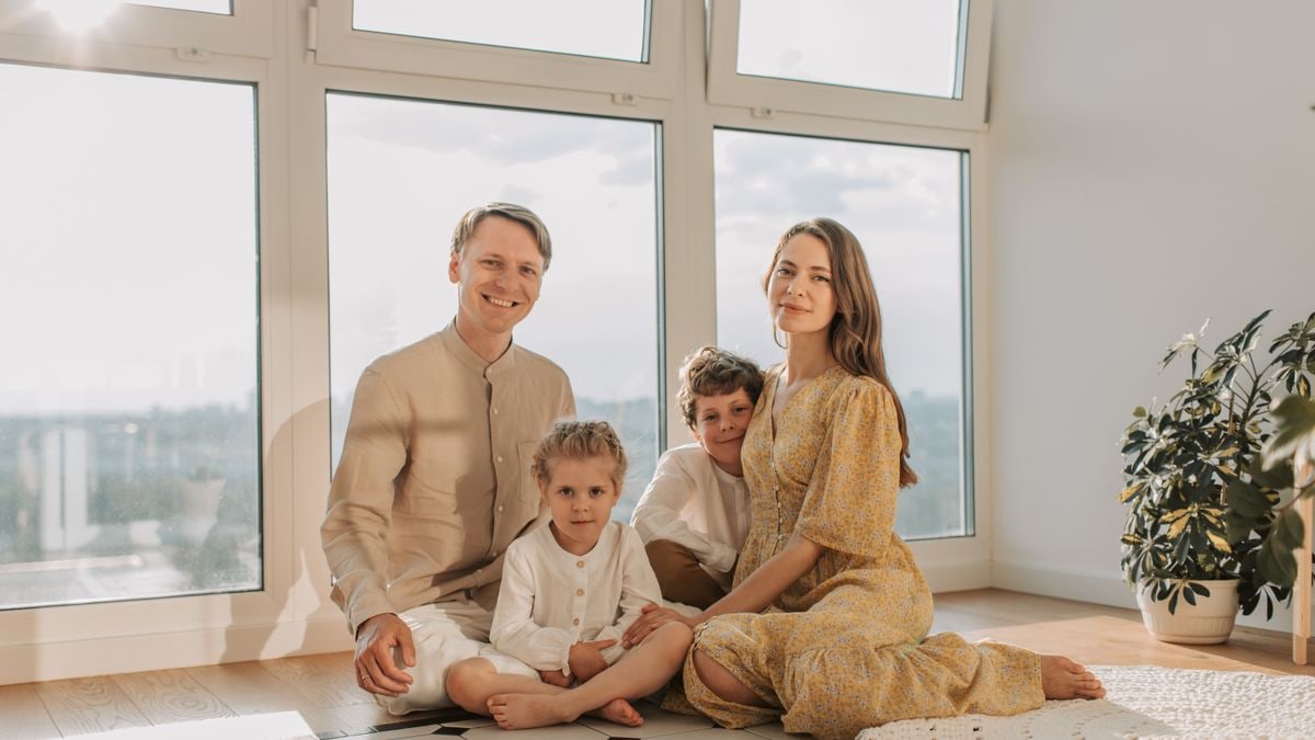A cheerful family of four sitting together on the floor of a sunlit living room.
