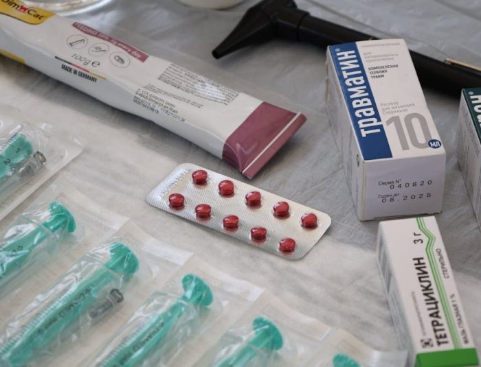 Flat lay of medical supplies including syringes, pharmaceuticals, and an otoscope on a table.